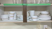 Corelle dishware including mugs, tea cups, bowls, plates stacked in a cabinet shelf.