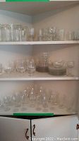 Three shelves filled with various Cornflower pattern glasses including tumblers, stemmed glasses, and small plates visible.