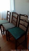 Three wooden dining chairs in a row showing carved ladder backs and padded seats of varying colors.