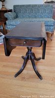 Side view of the vintage drop leaf side table showing claw feet, pedestal base, and single drawer