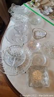 Overview of multiple clear glass serving plates and bowls arranged on table, showing various shapes and textures