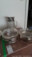 Photo showing the silver plated crystal water jug with ornate handle and lid, along with two silver plated covered casserole dishes with glass lids.
