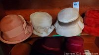 Four ladies hats displayed on shelf, peach, white, beige bucket style, and red fur textured hats visible