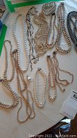 Photo showing multiple imitation pearl necklaces in various colors and lengths laid out on a surface, including a beaded bracelet.