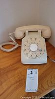 Full view of cream-colored rotary dial phone with handset on wooden surface.