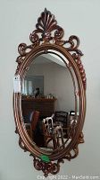 Full front view of the oval wall mirror showing the ornate bronze plastic frame and reflective glass.