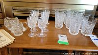 Eight stemmed liqueur glasses, eight tumblers, cream pitcher, sugar bowl arranged on table.