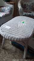 Full view of the white wicker coffee table in a room with other wicker furniture and floral cushions.