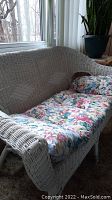 Side angle view of the white wicker love seat showing floral cushion and some wrapping missing on legs.