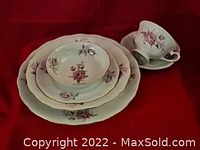 Stacked dinnerware showing the rose pattern on plates, bowls, and a cup with saucer