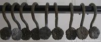 Front view of the set of 8 metal curtain hooks hung on a rod, showing the flower-shaped decorative ends with oxidation and wear.