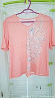 Peach short sleeve top with bead and rhinestone floral decoration on front.