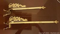 Pair of antique Victorian curtain rods laid flat, showing decorative leaf design and worn cream-yellow paint with rust and scratches.