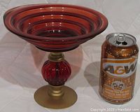 Red and gold glass display dish beside a soda can for size reference on a white background.
