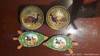 Four decorative Italian ceramic plates and dishes, two round painted plates of peacocks on gold mosaic background, and two green cactus leaf shaped dishes with donkey cart scenes.