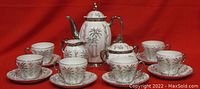 Porcelain espresso coffee set arranged with pot, sugar bowl, cream pitcher, 6 cups and saucers against red background, showing palm tree motif and silver trimming.