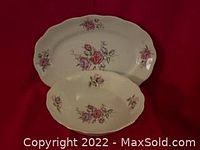 Two white porcelain serving platters with pink and violet rose floral patterns and gold trim, displayed on red background.