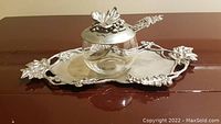 Pewter sugar bowl with decorative lid on matching tray with spoon featuring grape motif set on wood surface