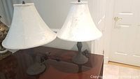 Pair of two decorative table lamps with white fabric shades placed on a table, showing overall condition and size.