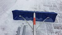 Blue plastic shovel head attached to aluminum handle, showing some wear on the edges.