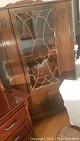 Front view of vintage china cabinet showing glass door with wooden grille and carved side panel.
