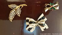 Three vintage costume jewelry brooches including a leaf design and two different bow designs shown from front.