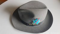 Grey felt fedora hat with black ribbon and blue/red feather detail
