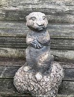 Front view of concrete otter sculpture on rock base outdoors with wood plank background.