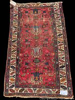 Full view of the rectangular handmade rug showing its central geometric and floral pattern in red tones with a decorative border.