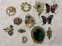 Full view of all 12 vintage costume jewelry pins arranged on a white fabric background, showing various designs including floral and butterflies.
