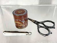 Photo showing cloisonne jar, sterling handle scissors, and mother of pearl pocket tool together.
