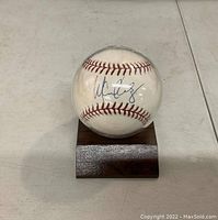 Baseball with Manny Ramirez's signature in blue ink shown inside the clear protective case on wooden base.