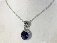 Close-up of the pendant showing the sapphire blue stone and detailed filigree bail.