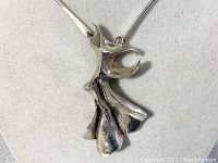 Close-up image of the sterling silver sculptural pendant, showing curved, abstract shapes with textured and smooth finishes.