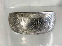 Front view showing engraved Tlingit formline motifs on polished silver surface