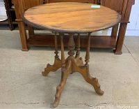 Full view of the antique round wooden top stand showing the round surface and the base with four ornately carved legs.