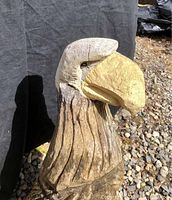 Front and side view of carved wooden bald eagle with detailed beak and feathers, showing weathered paint and some cracks.