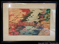 Framed vintage Japanese print showing red bridge over river with autumn foliage and two figures with umbrellas.