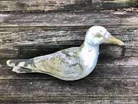 Side angle of concrete seagull sculpture showing full body, painted white and gray with weathering and grime.