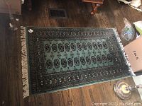 Full view of rectangular area rug on hardwood floor, green background with repeating medallions and fringe
