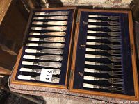 Top view of wooden box open displaying twelve fish knives on left and twelve fish forks on right in blue velvet lining