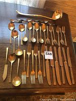 Full layout of flatware set on wooden table showing dinner forks, spoons, knives, cocktail spoons and ladle.