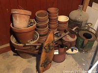 Overall view of terracotta pots, two red watering cans, green metal container, decorative wood slice and stacks of small pots