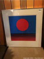 Full view of the framed print leaning against a wood-paneled wall, showing overall condition and framing.