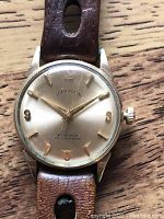 Front view of silver-tone dial with gold-tone markers and applied Arabic numerals on brown leather band