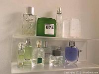 Full view of seven men's cologne bottles on two clear shelves with a green box, showing variety of styles and brands.