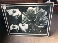 Full view of framed black and white floral lithograph leaning against wooden cabinet, showing front of frame and artwork