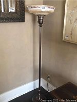 Full view of the standing torchiere floor lamp showing metal base and decorative glass shade.