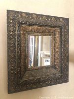 Frontal view of rectangular vintage mirror with wide embossed frame showing detailed floral and scrollwork.