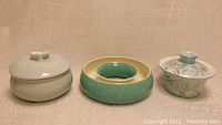 Set of three pottery pieces: blue covered pot with gold floral design, green ring-shaped pottery, and another blue covered pot with raised blossom lid.